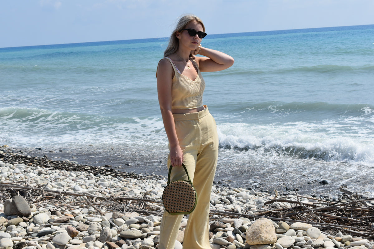 ILHA Olive Francesca handbag held by model, beach and sea background